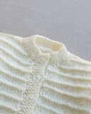Close-up of a light green knitted garment with button details on a gray background