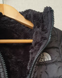 Close-up of a black puffer jacket with a wooden hanger on a light gray background
